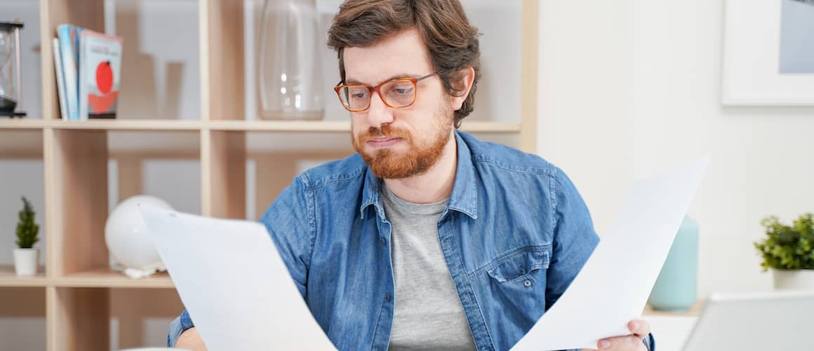 Troubled young man looking at paperwork and worrying.