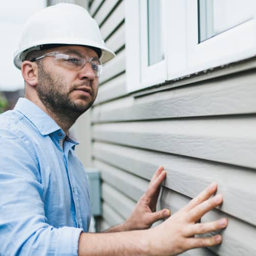 An image showing a building inspector checking windows of a building, related to an article or content discussing inspection or regulatory compliance.