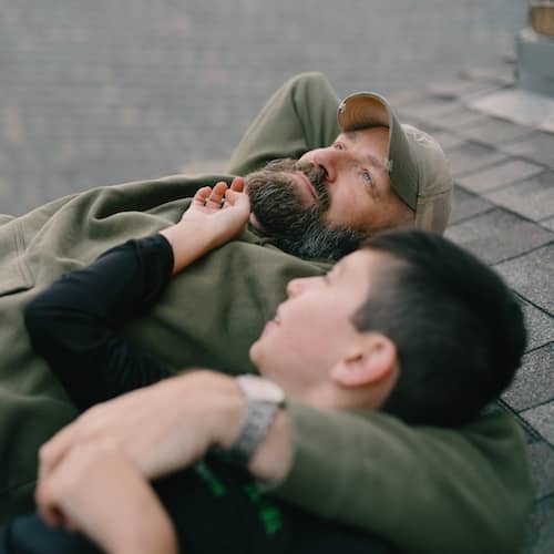 Dad holding son while they lay on roof.
