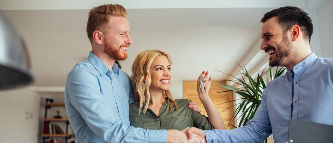 Couple receives the keys to their new home, smiling and shaking hands with their real estate agent. Woman holds up the keys.