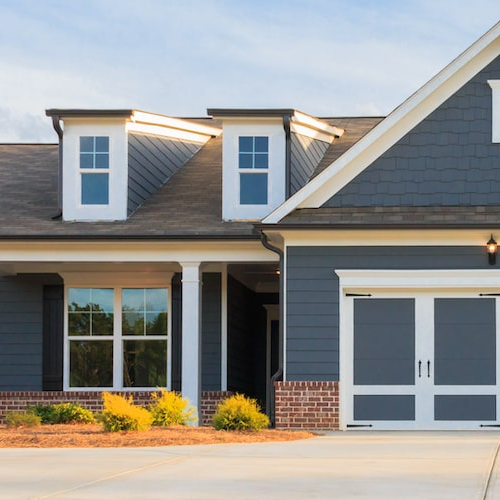Exterior view of a gray ranch-style home with a driveway and surrounding greenery.