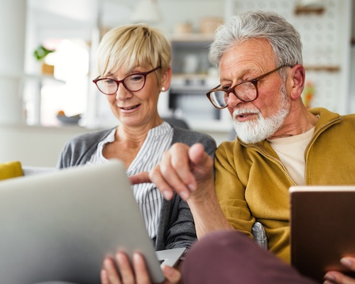 Senior couple sitting on a couch at home with a laptop and book.