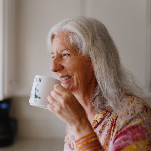 Woman drinking coffee and smiling in the kitchen.