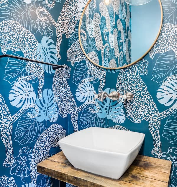 Half bathroom with a basic sink, mirror, and ornate blue wallpaper.