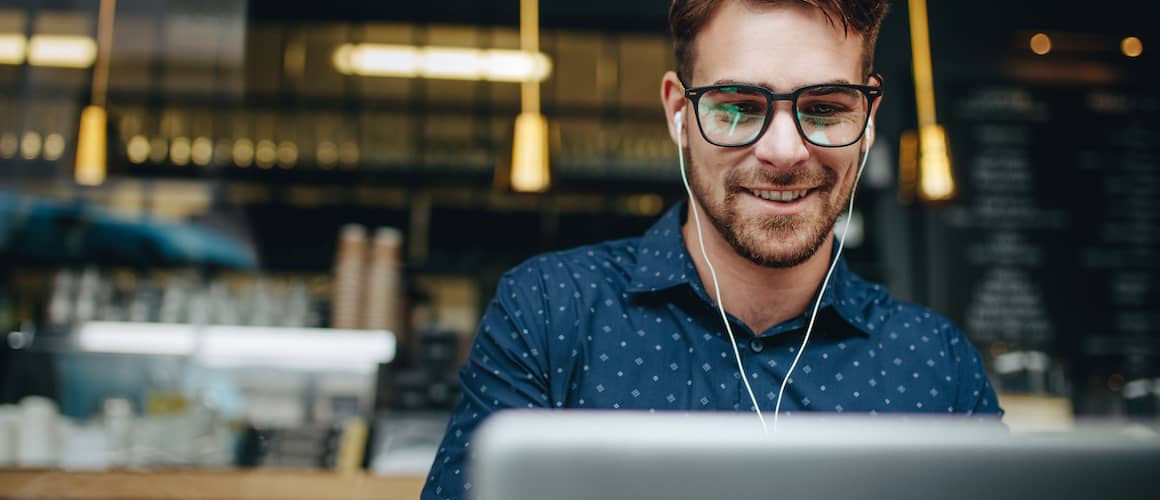 Image of man outside coffee shop, smiling at personal loan options on laptop screen.