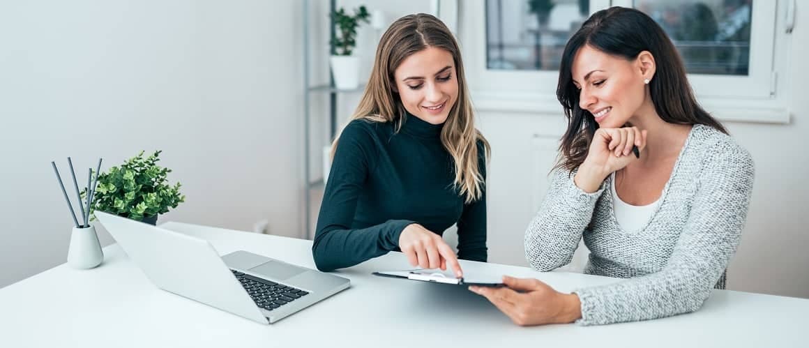 Two women going over paperwork in an office setting, potentially related to real estate or finances.