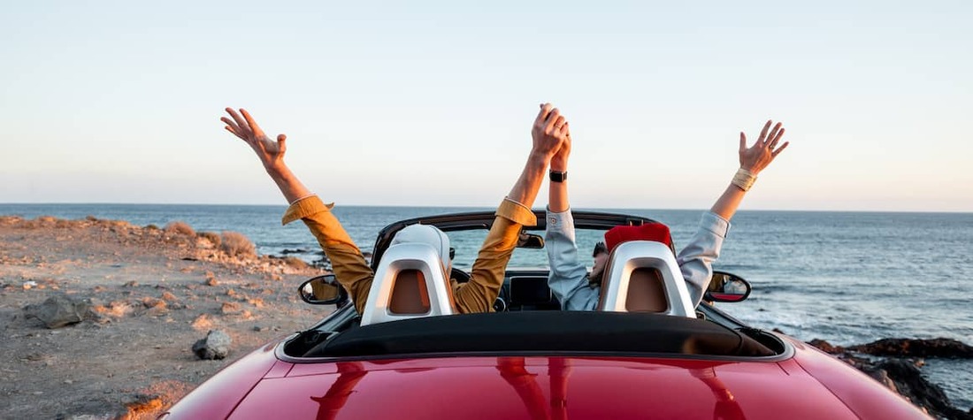 Couple driving expensive car oin the beach.