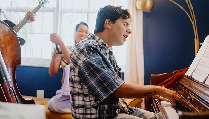 Man playing piano and singing while people play instruments in the background.