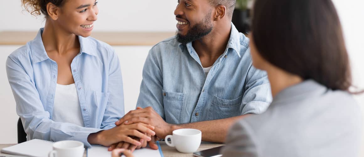 Couple in their early thirties looking at one another smiling, sitting across from a financial advisor.