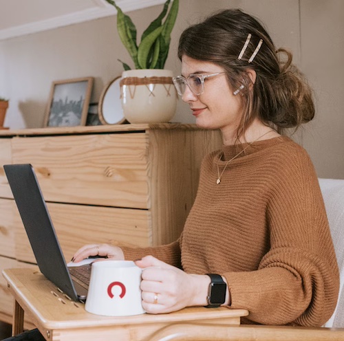 Young woman at laptop while drinking from Rocket company mug.