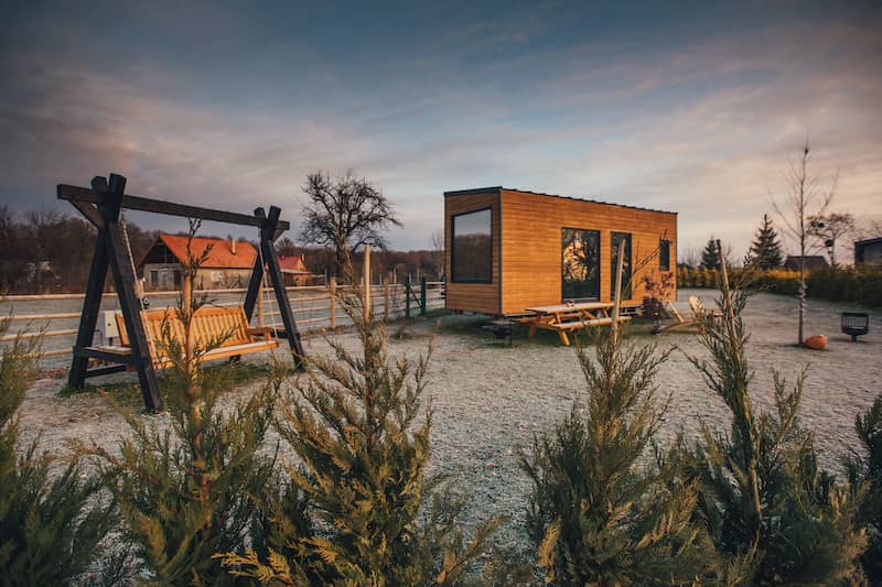 Tiny house on a sandy lot in the southwest with a bench swing at sunset.