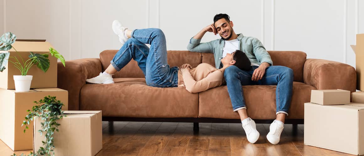 Couple in new rental relaxing on couch with unpacked boxes around them.