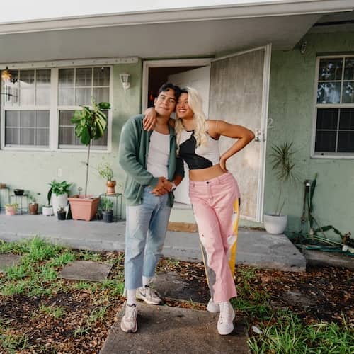 Two young people smiling from the front of their home. 
