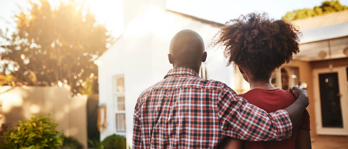 Young couple standing before a new house at sunset.