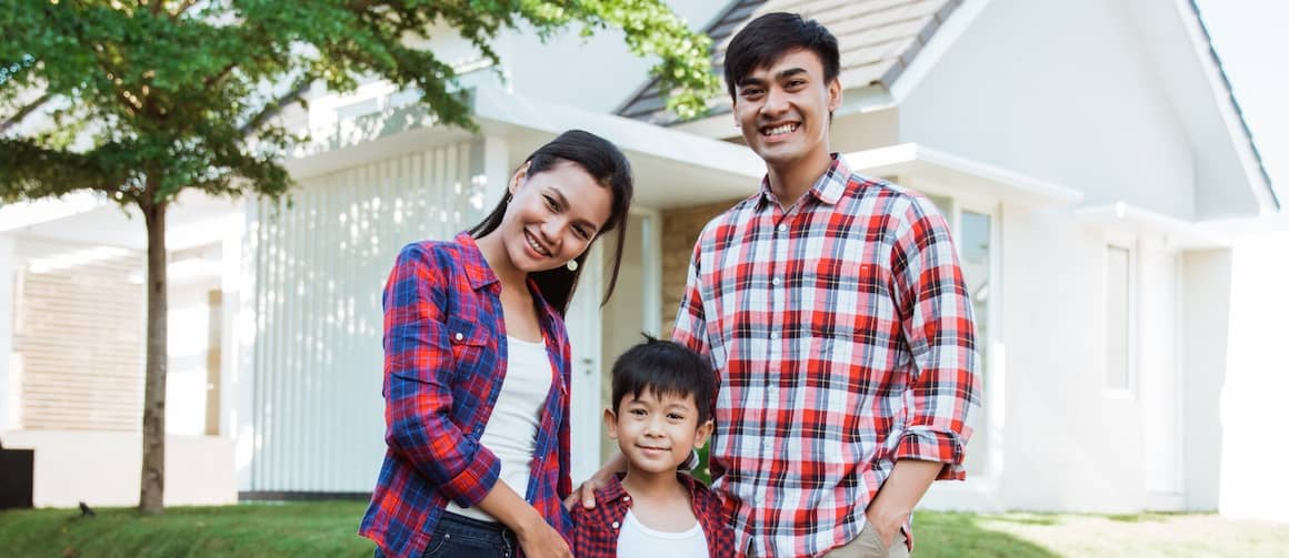 Family with young boy smiling in front of new home.