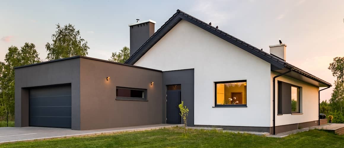 Sleek, modern home in white with brown trim and a solid brown garage at dusk. 