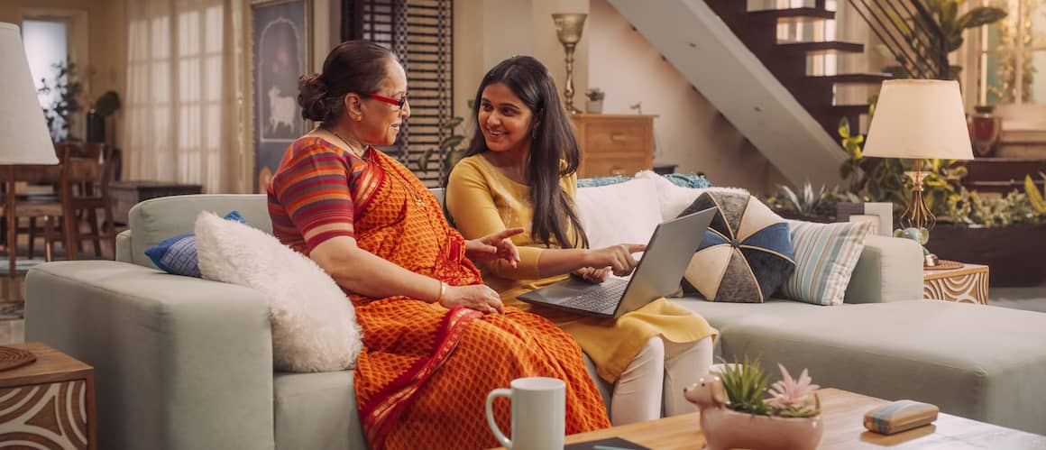 Senior woman helping daughter choose a home online as they sit in the mother's living room.