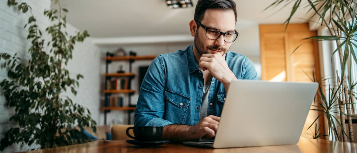 Man looking pensive at laptop, resting chin on his hand.