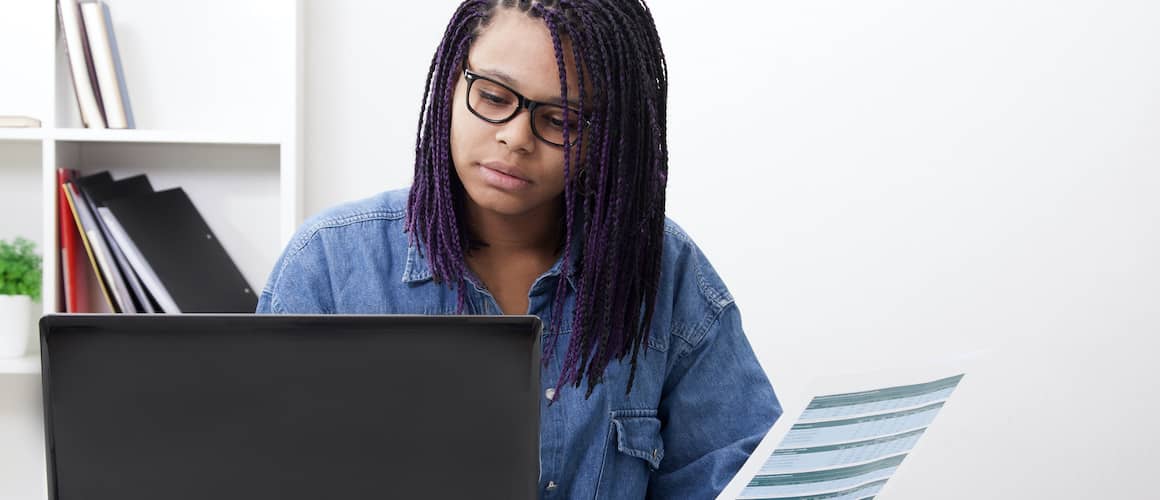 A woman on a computer holding paper, potentially representing a person handling paperwork or administrative tasks.