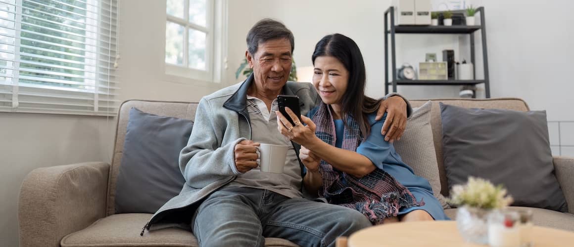 Older couple sitting on a couch together and looking at a cell phone.