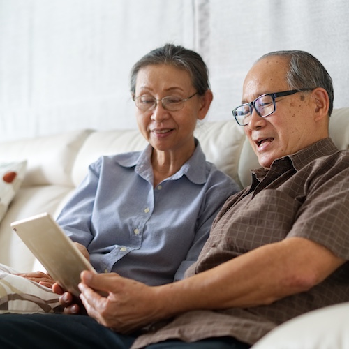 Senior couple sitting on sofa in home with a tablet and relaxing together.