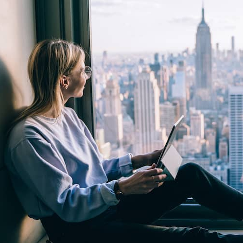 A woman standing and looking at a cityscape with tall buildings and skyscrapers in the background.