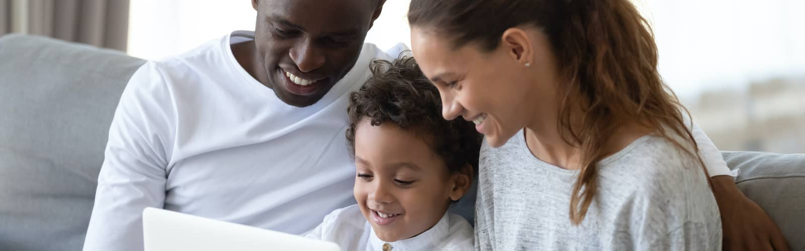 Happy family gathered around laptop on couch enjoying their time.