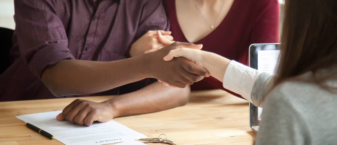 Mixed race couple shaking hands with real estate agent.