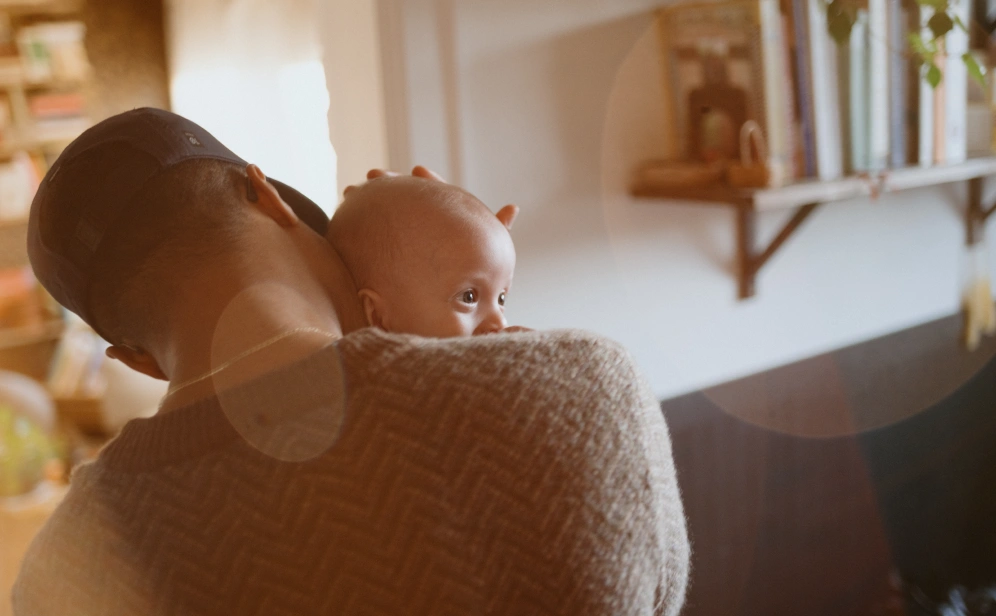 The back of a man holding his baby in their living room.