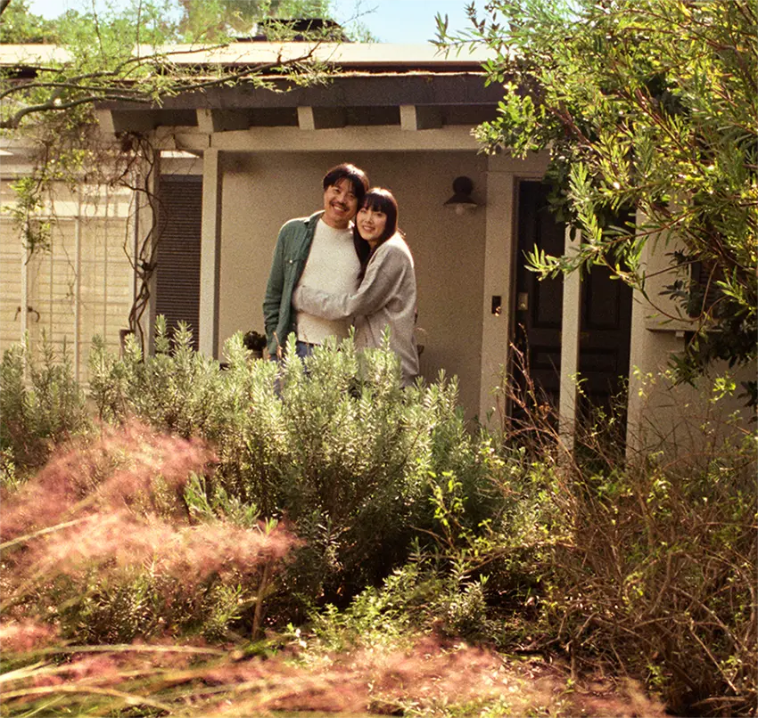 An Asian couple stands in their backyard garden of their new home.