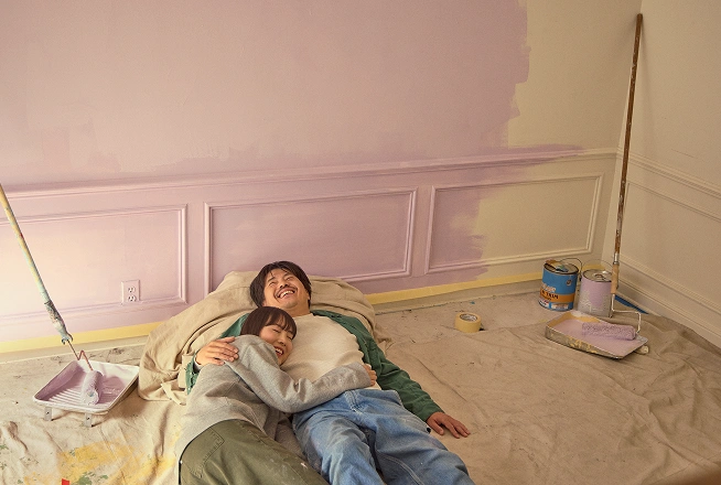 An Asian couple takes a break while laying on the floor of the room they are painting in their new home.