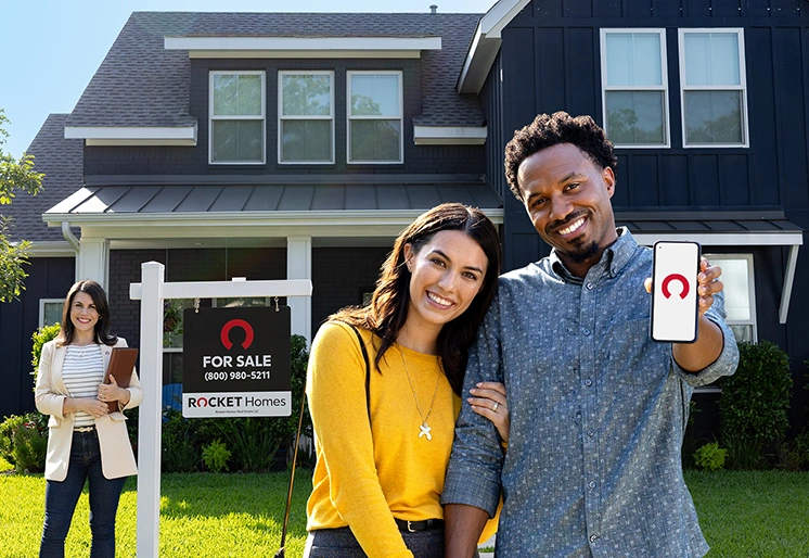 A happy thirty-something Black man and his wife just made an offer on a gray home with white trim with help from Rocket Mortgage and their Rocket Homes real estate agent.