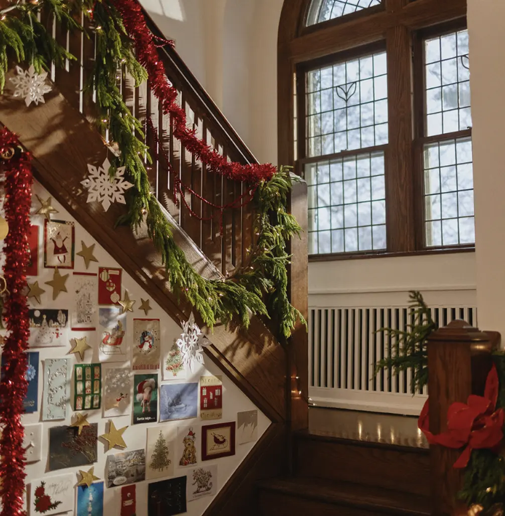 An interior view of a home with a window and staircase displaying holiday garland and greeting cards.