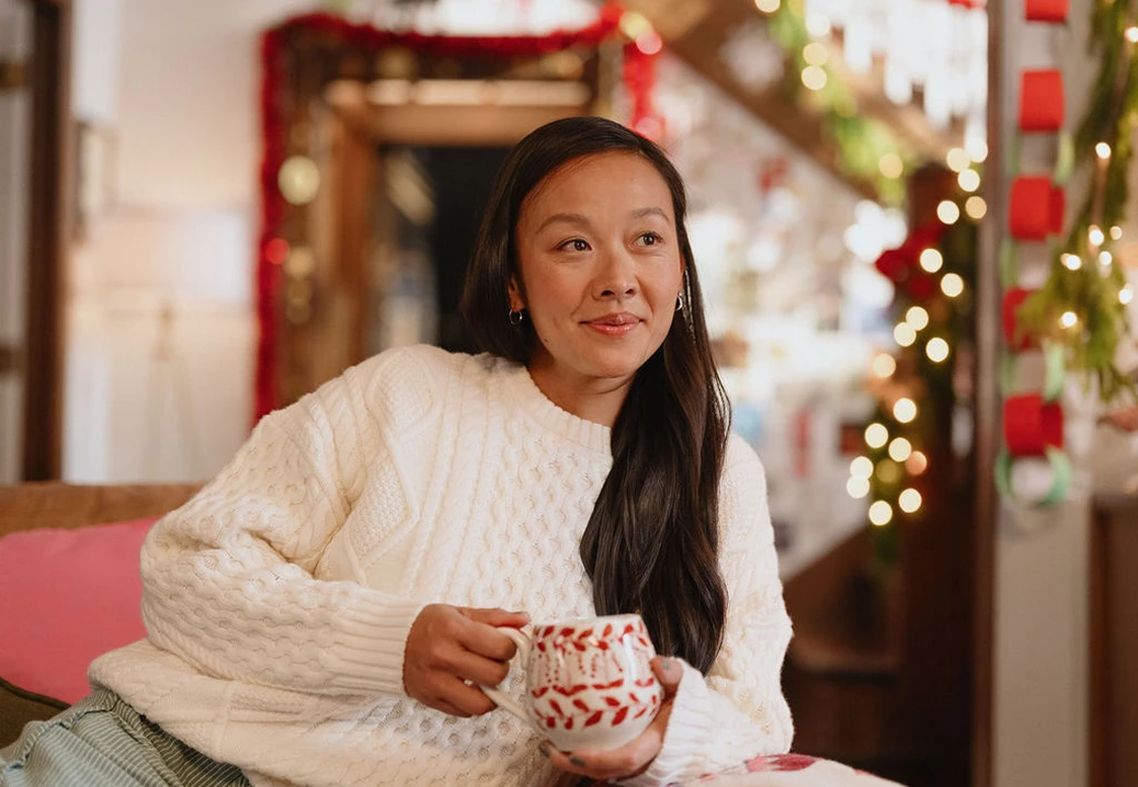 A person sitting indoors with a patterned coffee mug in a holiday-decorated room.