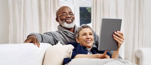 A middled-aged black man with a white beard and his wife use their devices to learn about how they can take cash out of their home by refinancing with Rocket Mortgage.