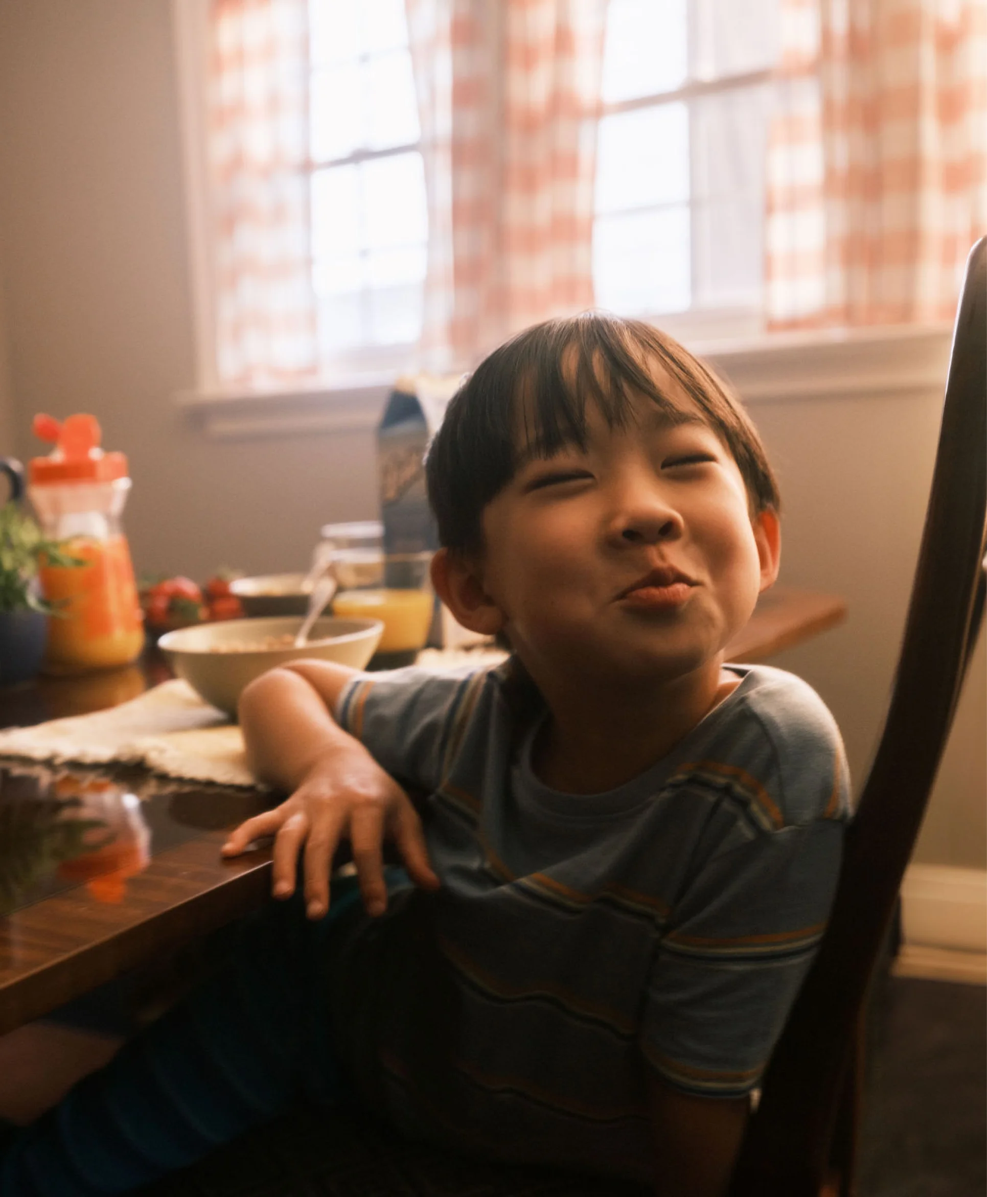 A young Asian boy takes a moment from eating breakfast to make a funny face.