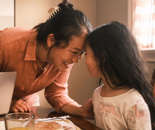 An Asian mom with her hair clipped back affectionately touches her forehead to her daughter's.