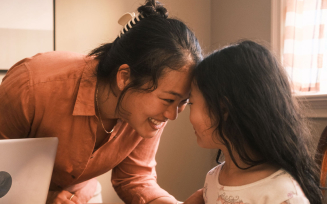 An Asian mom with her hair clipped back affectionately touches her forehead to her daughter's.