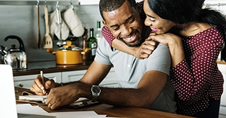 An African American man and woman embracing while budgeting in their kitchen.