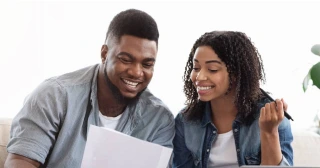 A Black couple in their 20s look at some papers while figuring out how much they need for a down payment on a home.