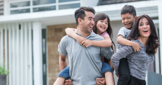 A mom and dad have fun giving their young kids piggyback rides outside their home.