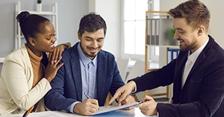 A mixed race man and woman talking with a mortgage lender while signing documents.