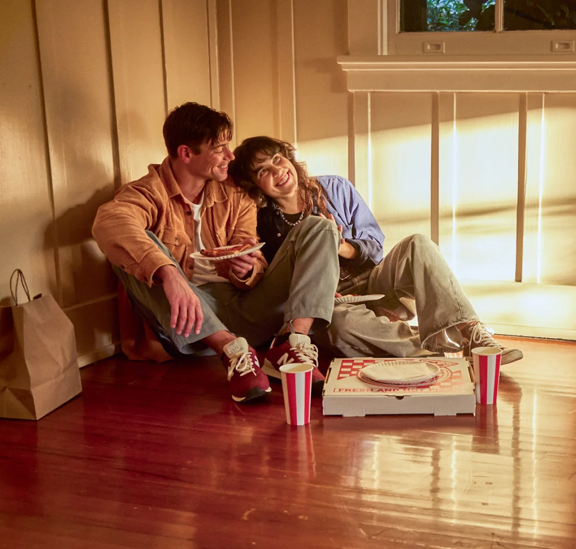 A smiling couple share take-out pizza on the floor of their new home discussing their plans for the future.