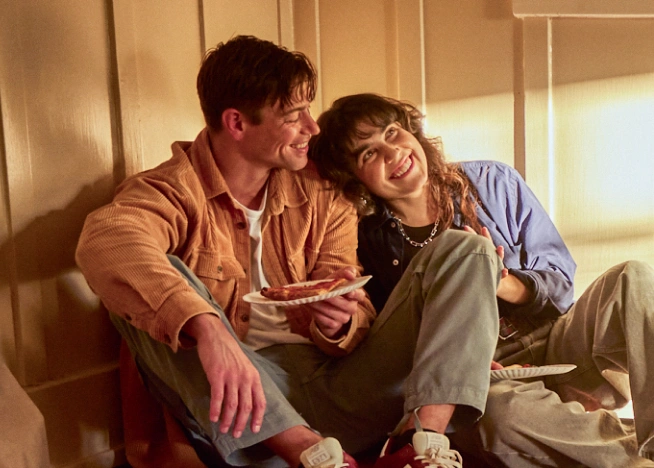 A smiling couple share take-out pizza on the floor of their new home discussing their plans for the future.