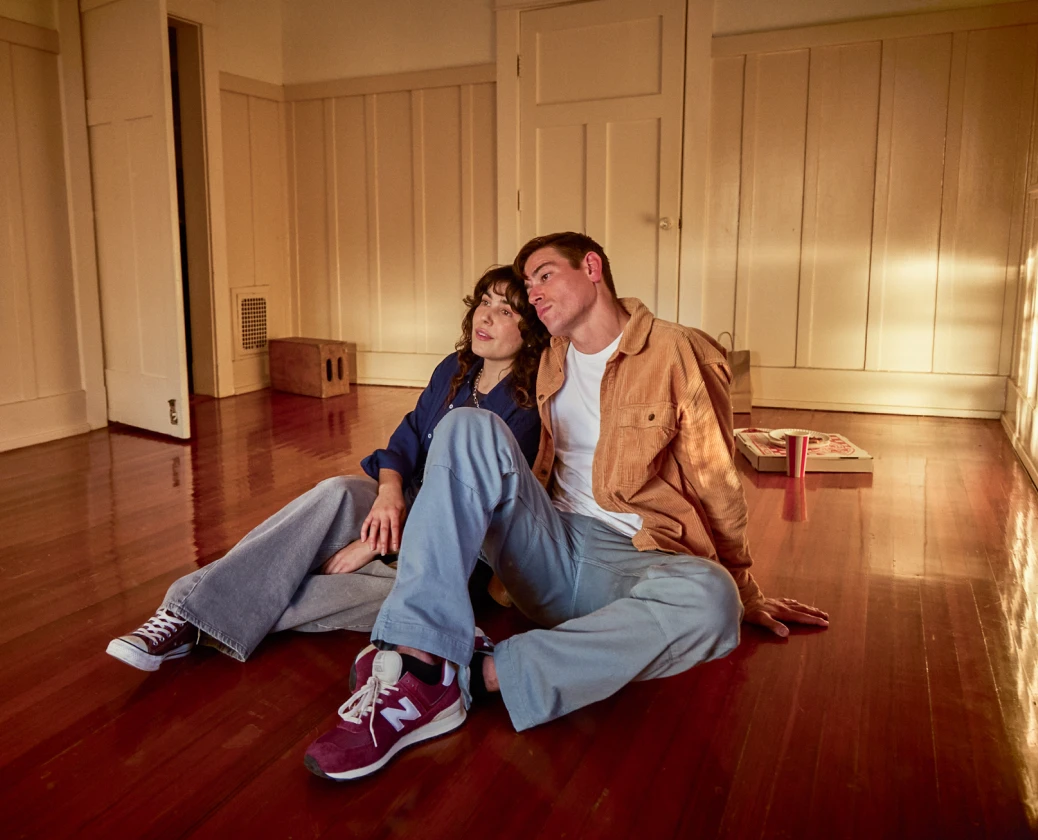 Down payment assistance can make buying a home possible for people like this couple in their 30s sitting in an empty room of their new home.