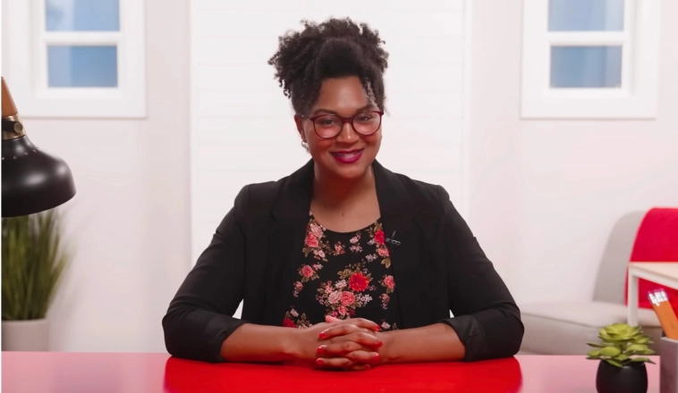 The Red Desk spokeswoman sitting at a red desk wearing a floral print shirt and black blazer.