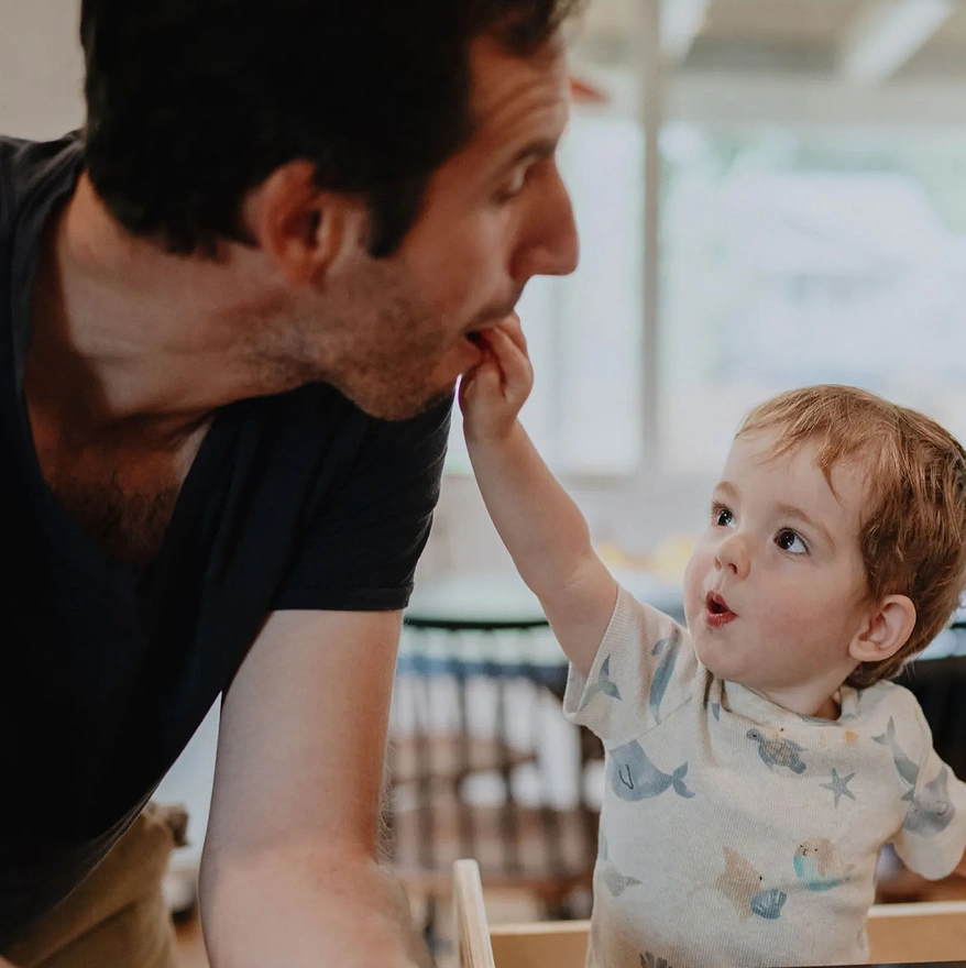 A baby playfully feeds his dad some food.