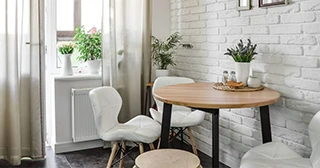 A Scandinavian-style compact dining room set with white chairs against a white brick wall.