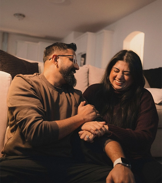 A husband and wife in their 30s share a loving moment together on the couch of their living room.