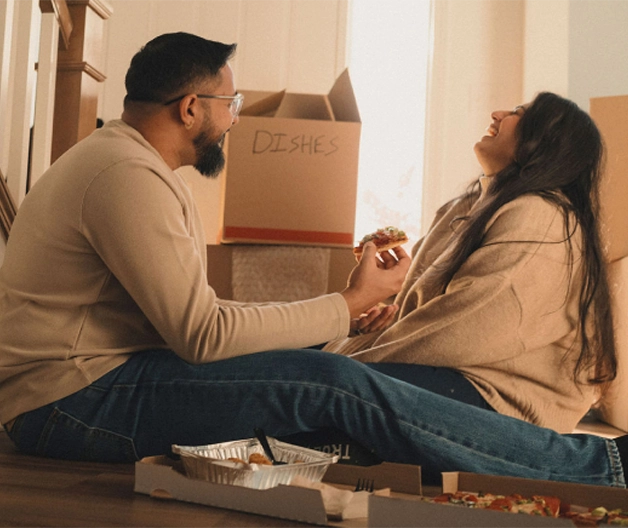 Two new homeowners enjoy a laugh over take-out pizza while taking a break from unpacking.